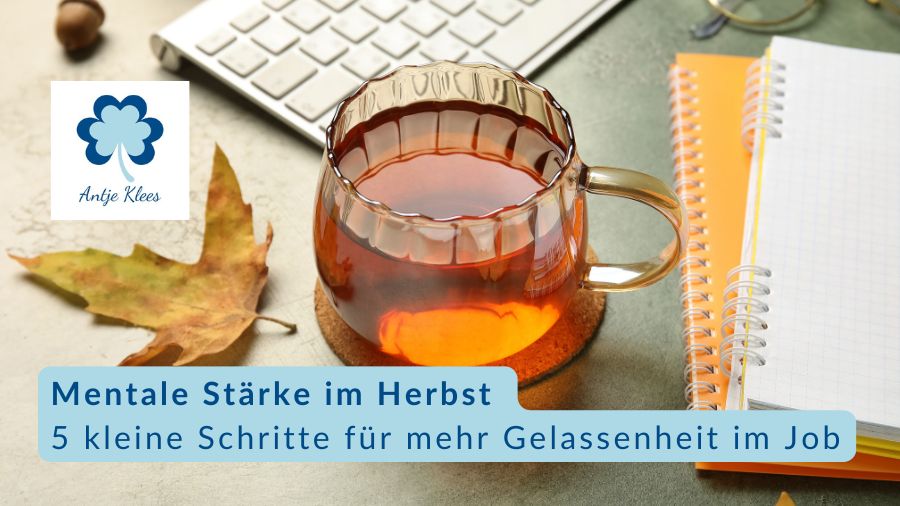 Eine Tasse Tee steht auf einem Schreibtisch mit Notizblöcken, einem herbstlichen Blatt und einer Tastatur.